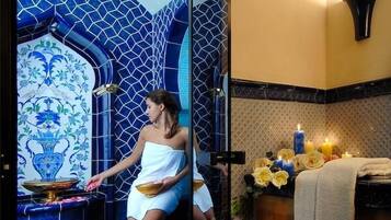 Relax in a serene spa room with a glass-enclosed seating area, featuring a blue-tiled wall and decorative tile design.