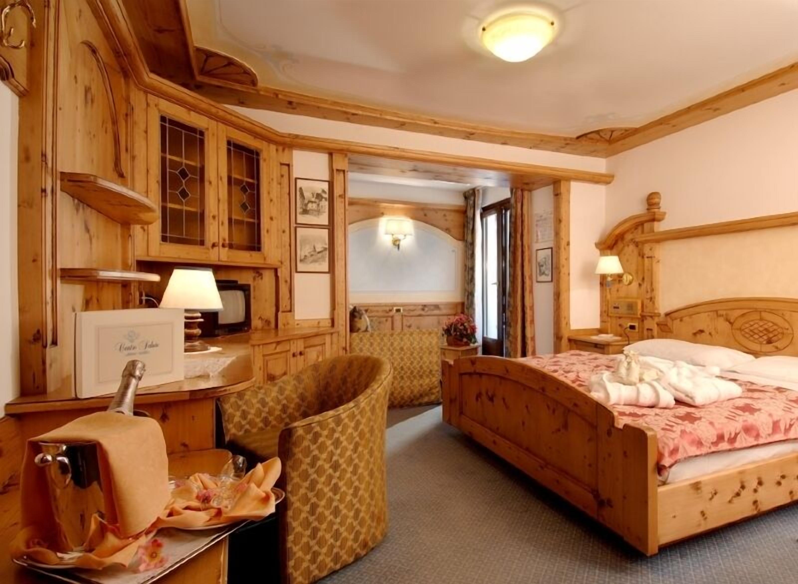 A wooden room with a bed, a chair, a table, and a television.