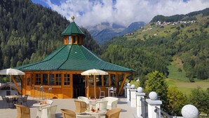 A wooden gazebo with a green roof and white chairs, overlooking a mountainous landscape. - Kristiania Pure Nature Hotel & Spa (Pejo)