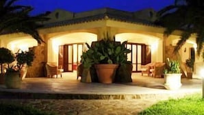 A well-lit building with a patio area, large potted plants, and a stone pathway leading to the entrance. - Disio Resort (Marsala)