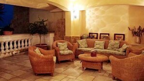 A spacious lounge area with wicker furniture, a stone floor, and a stone wall. - Disio Resort (Marsala)