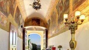 A hallway with ornate ceiling frescoes, a chandelier, and a candelabra.