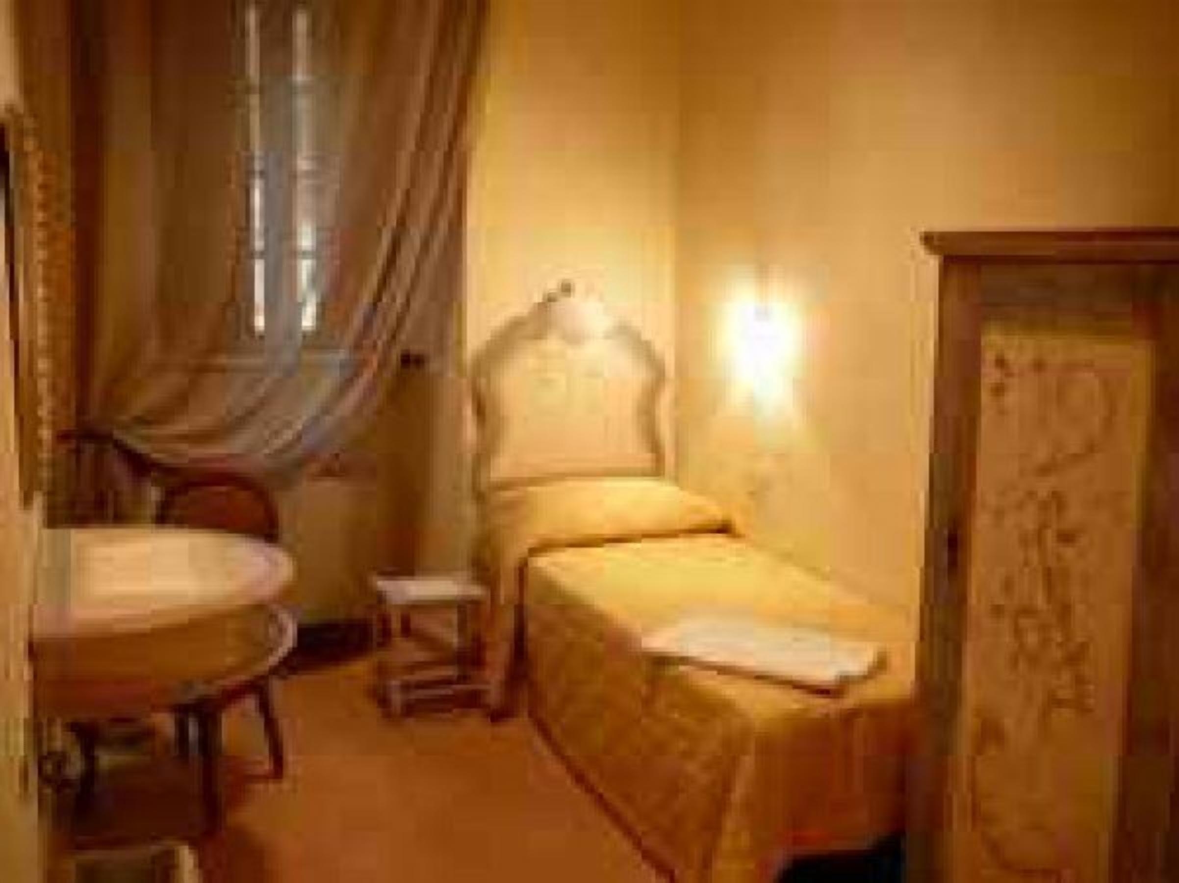 A small, cozy room with a single bed, a bedside table, a chair, and a window with curtains.