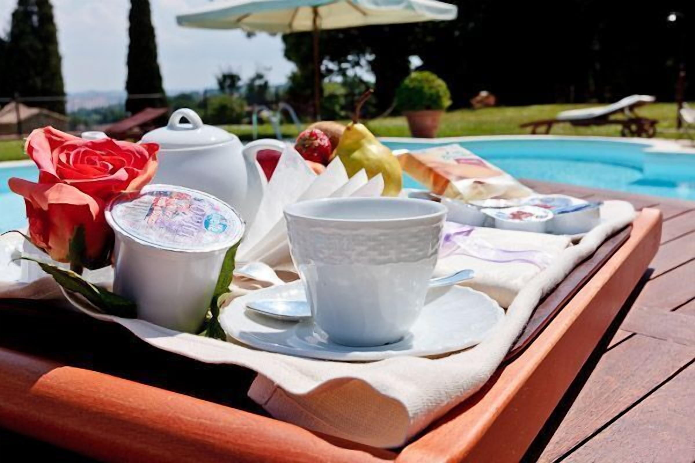 A tray with a teapot, cups, and a rose on a wooden table by a pool.
