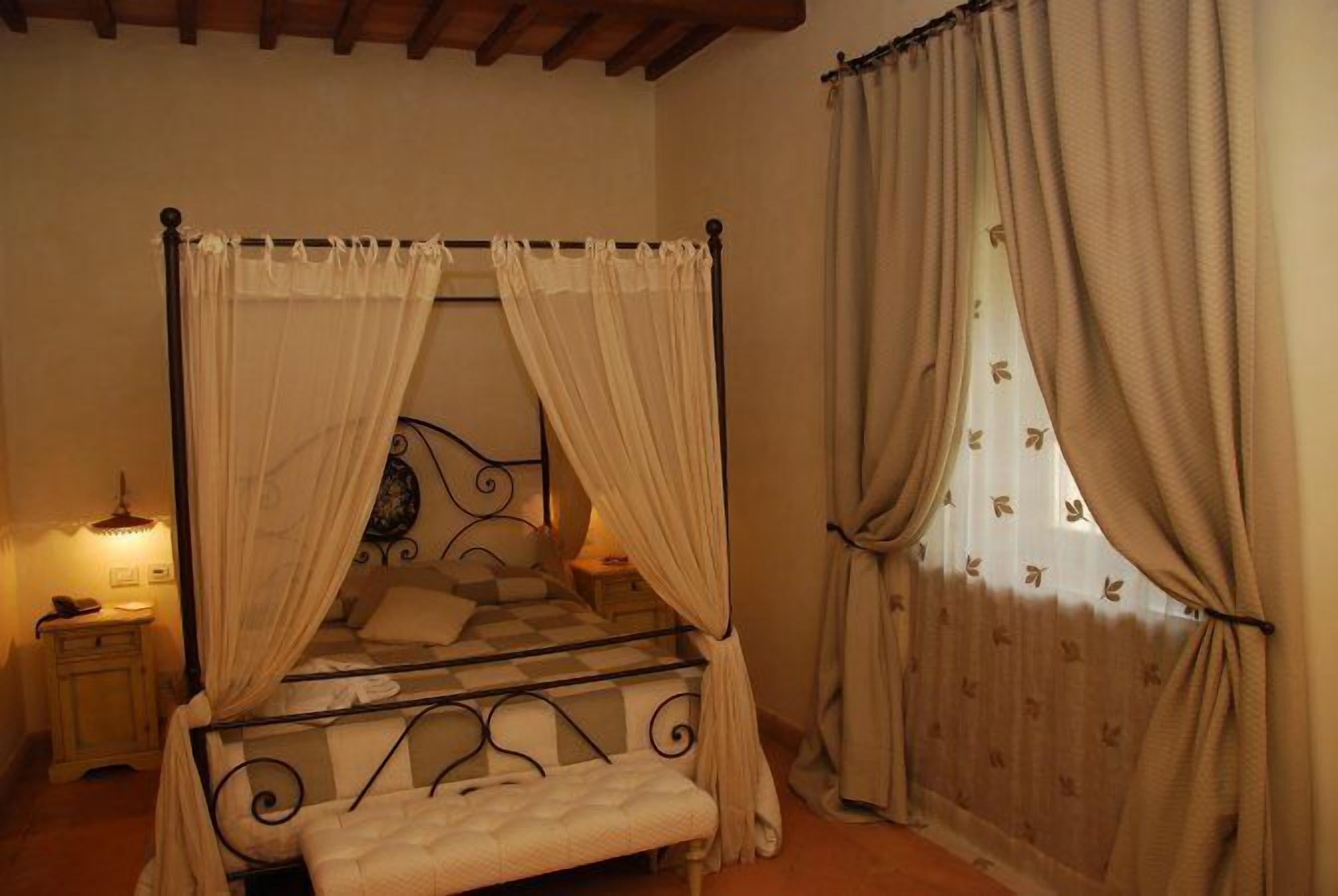 A four-poster bed with a checkered bedspread, a bedside table with a lamp, and a window with curtains.