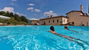 A swimming pool with lounge chairs and umbrellas, surrounded by a building with a tiled roof.