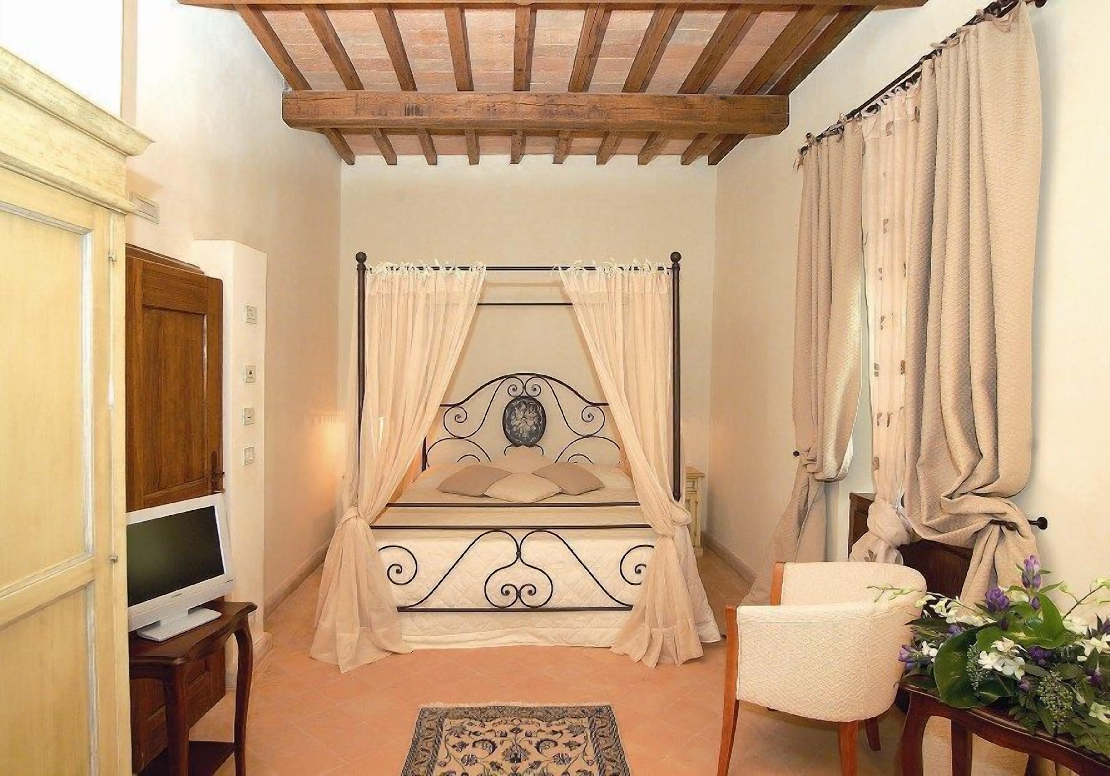 Un dormitorio con cama con dosel, un televisor sobre un soporte de madera, una silla y una mesita con una planta.