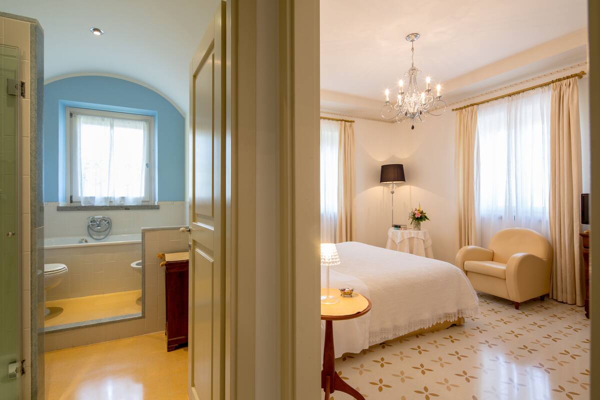 A hotel room with a bathroom, a bed, a chair, and a table.