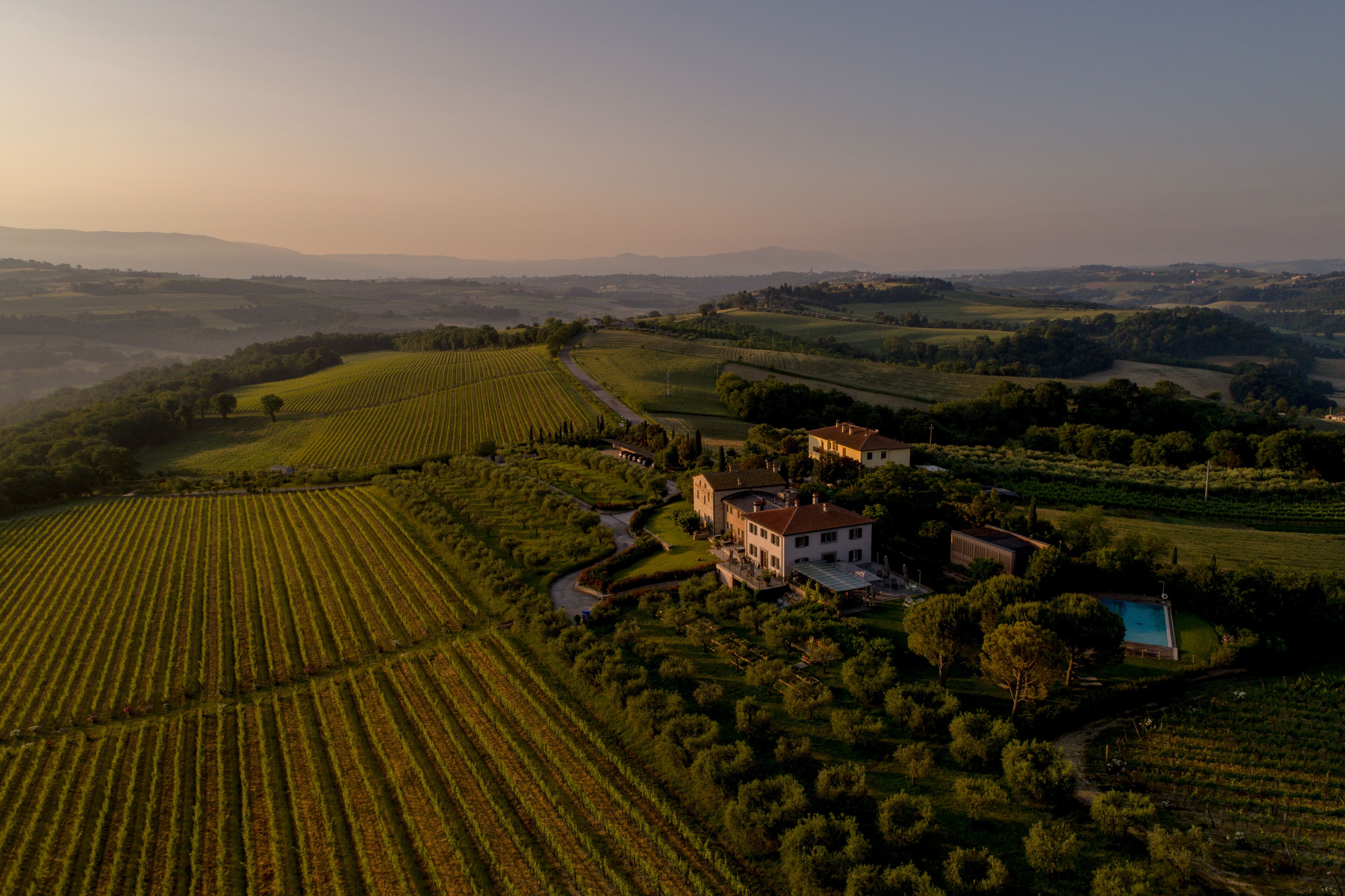 An aerial view of a countryside estate with expansive fields, a large house, and a swimming pool.