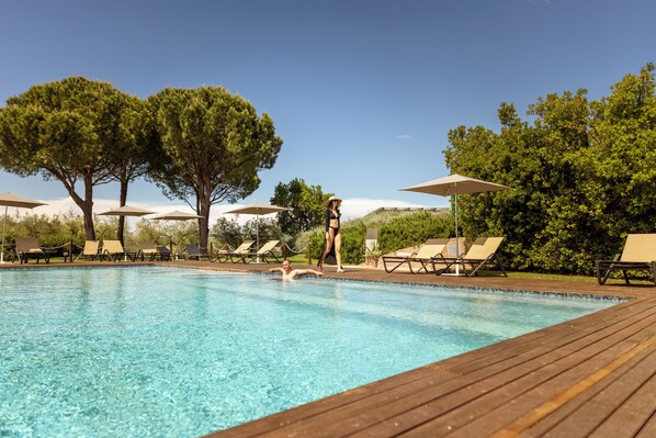 A swimming pool with lounge chairs and umbrellas, surrounded by trees.