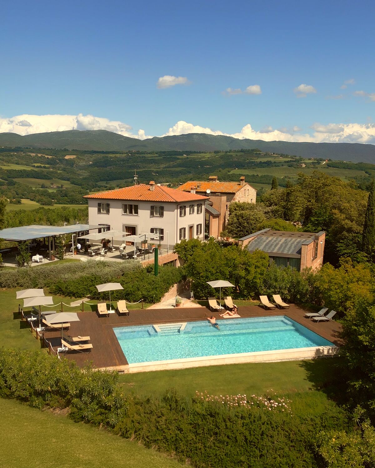 A large villa with a swimming pool, surrounded by lush greenery and mountains in the background.