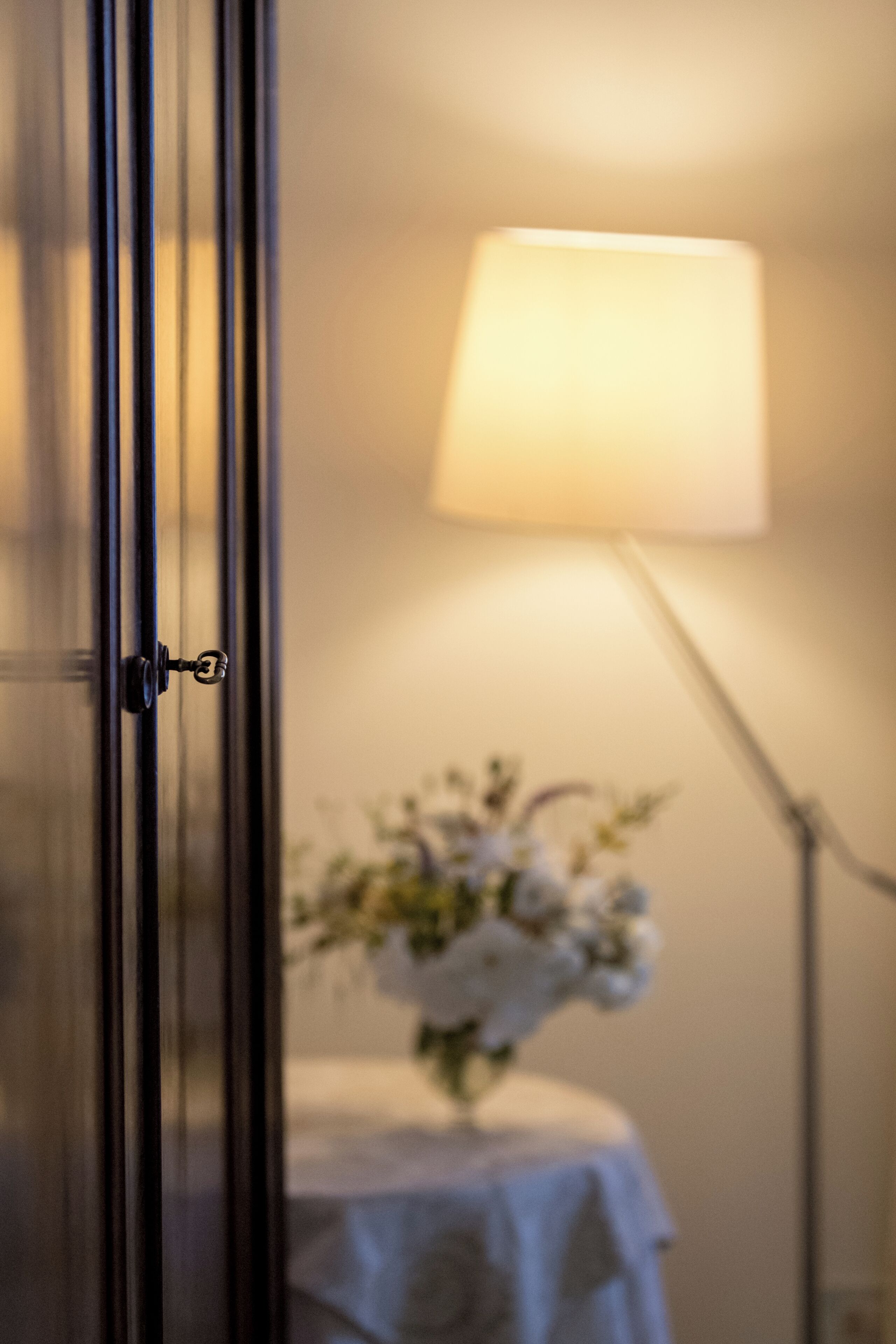 Una habitación con la puerta cerrada, una lámpara de noche y una mesita con un florero.