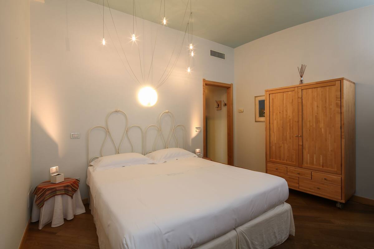 A bedroom with a bed, bedside table, wardrobe, and a hanging light fixture.