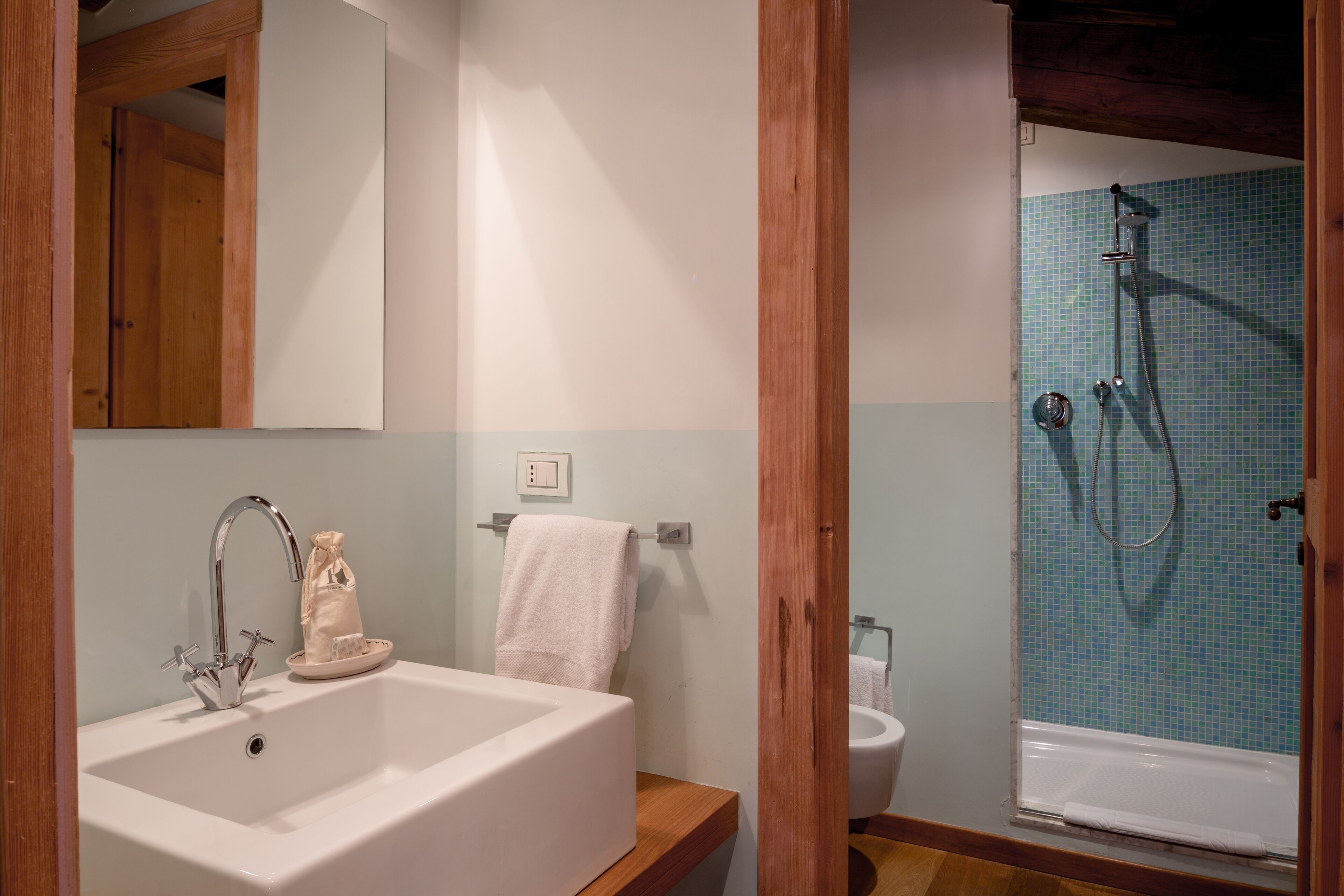 Un baño con un lavamanos blanco, un espejo, una ducha con pared de azulejos azules y vigas de madera.