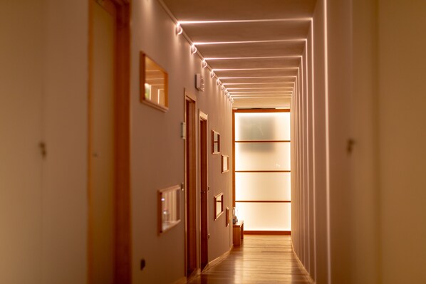A hallway with wooden floors and walls, framed pictures, and a lighted ceiling.