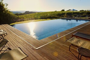 A wooden deck with a swimming pool, lounge chairs, and a view of a vineyard.