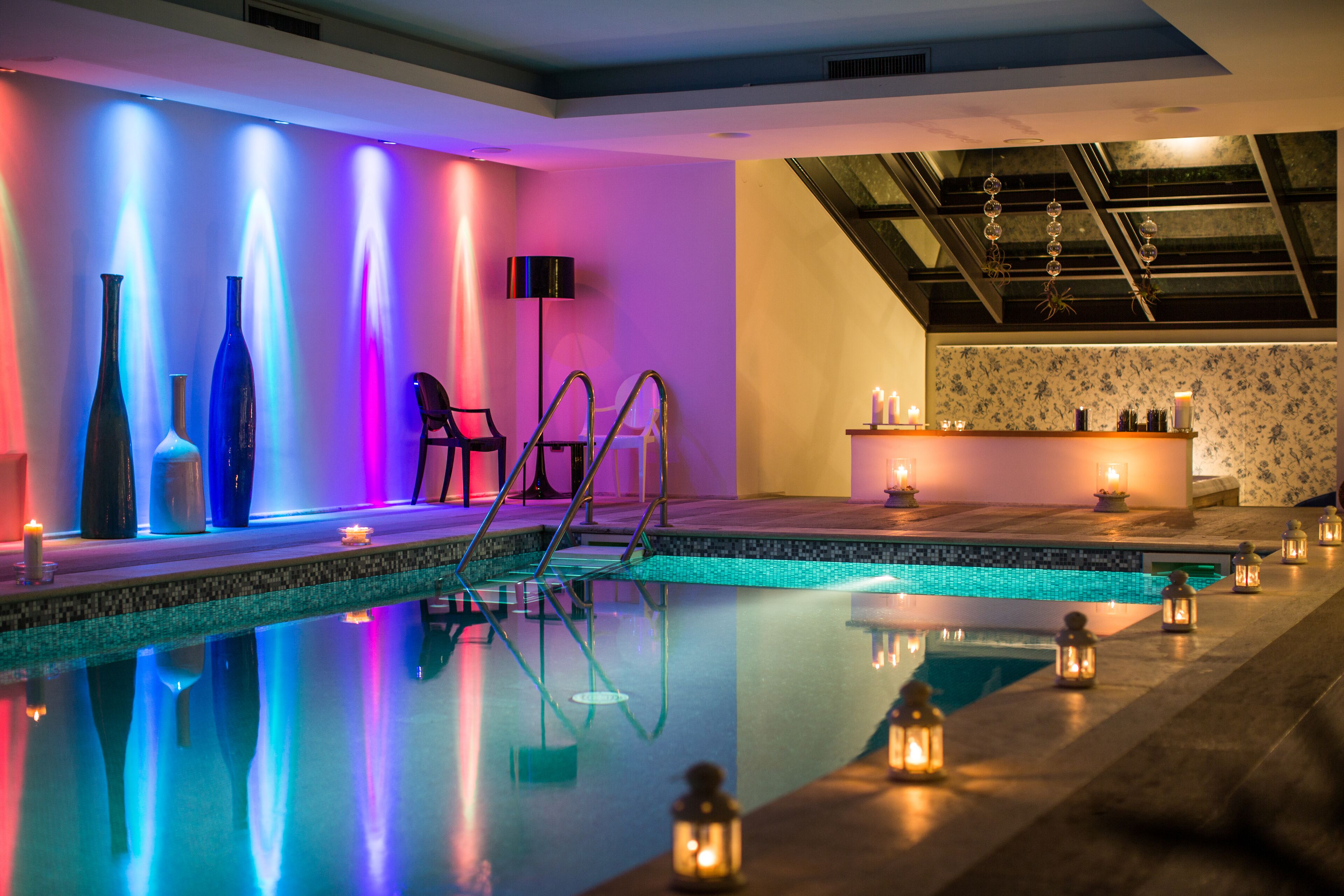 Un área de piscina interior moderna con una barrera de vidrio transparente, iluminación ambiental y jarrones decorativos.