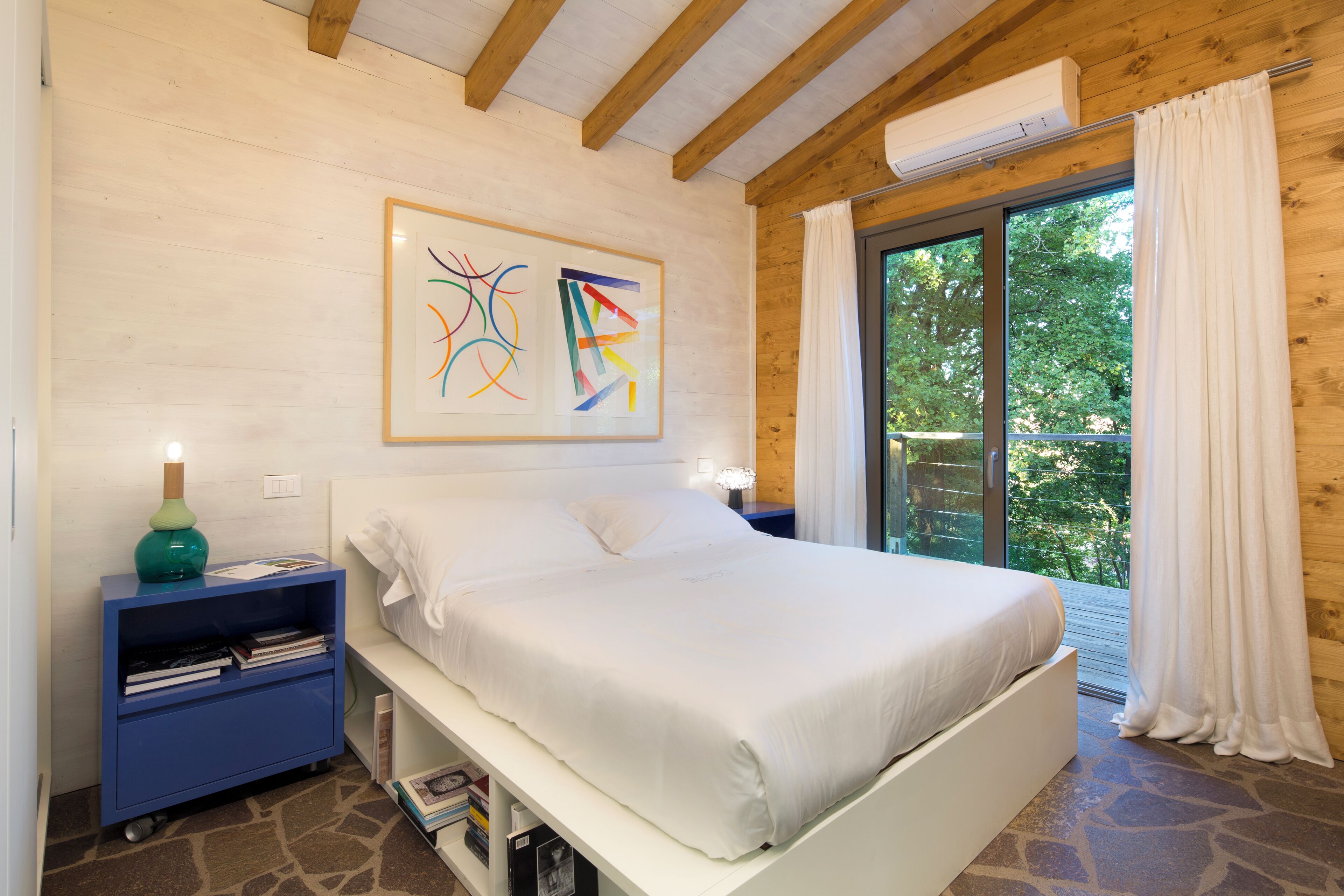 A bedroom with a bed, a nightstand, a bookshelf, and a window with curtains.