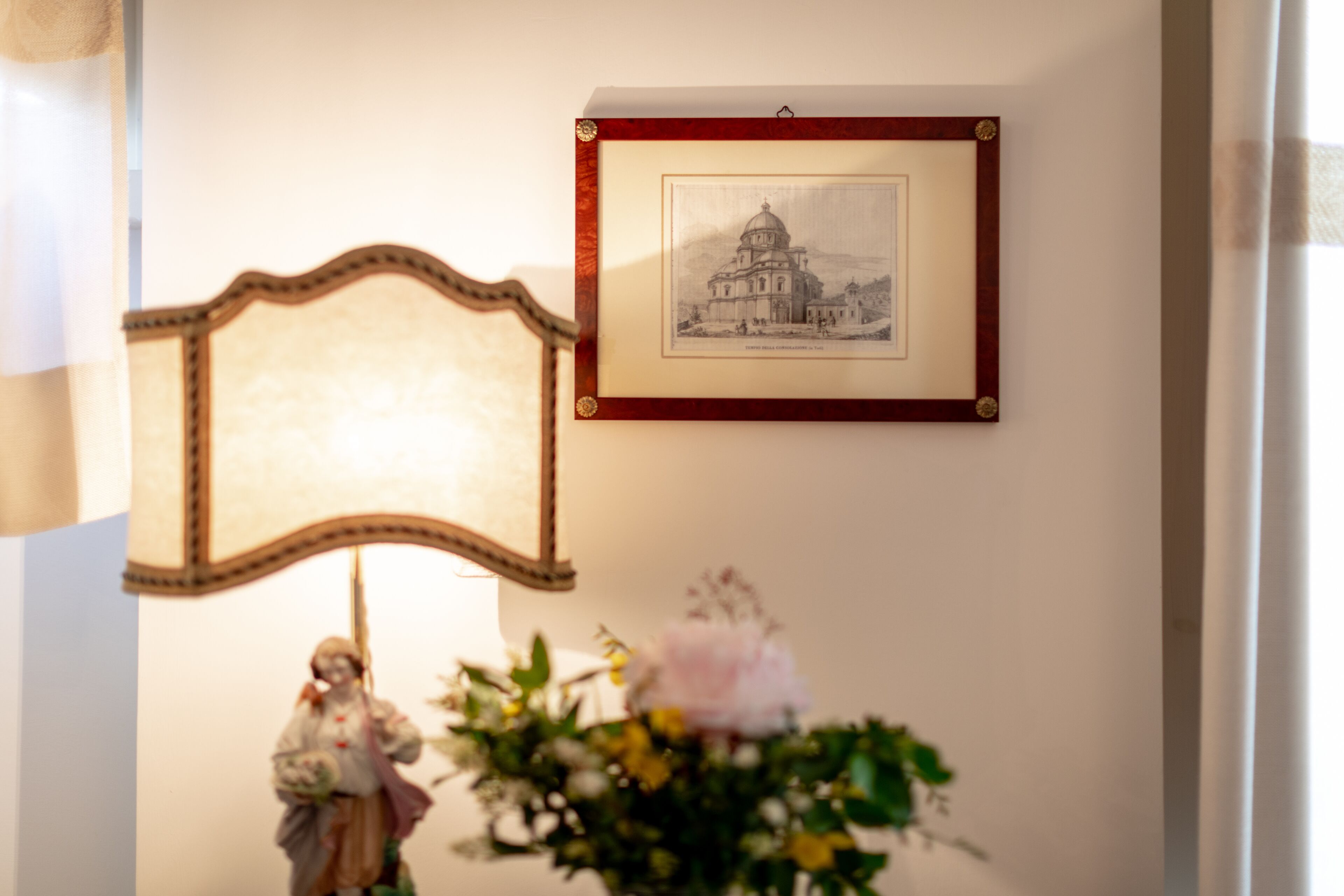 A framed picture of a building on a wall, a decorative mirror, and a statue with flowers.