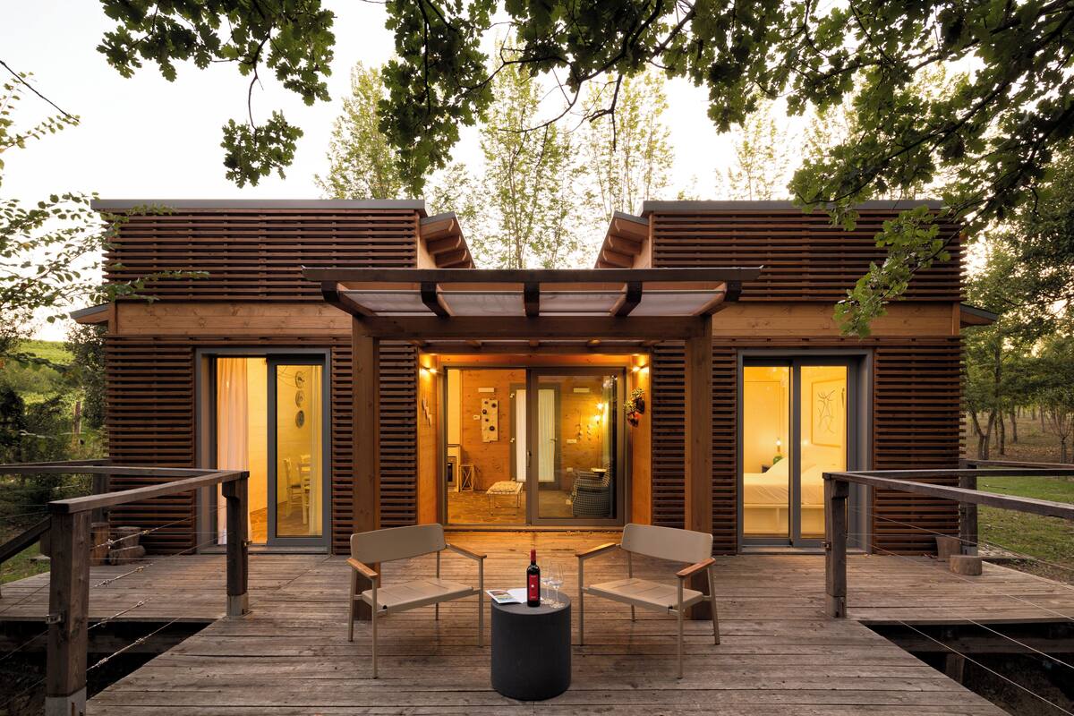 A modern wooden building with a deck, two chairs, and a table with a bottle.
