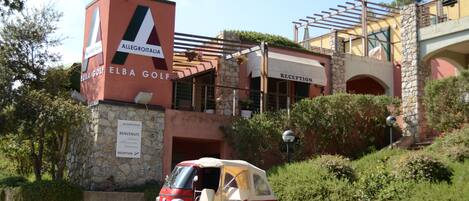 Un carrito de golf rojo y blanco estacionado frente a un edificio con fachada de piedra y un letrero que dice "ELBA GOLF".