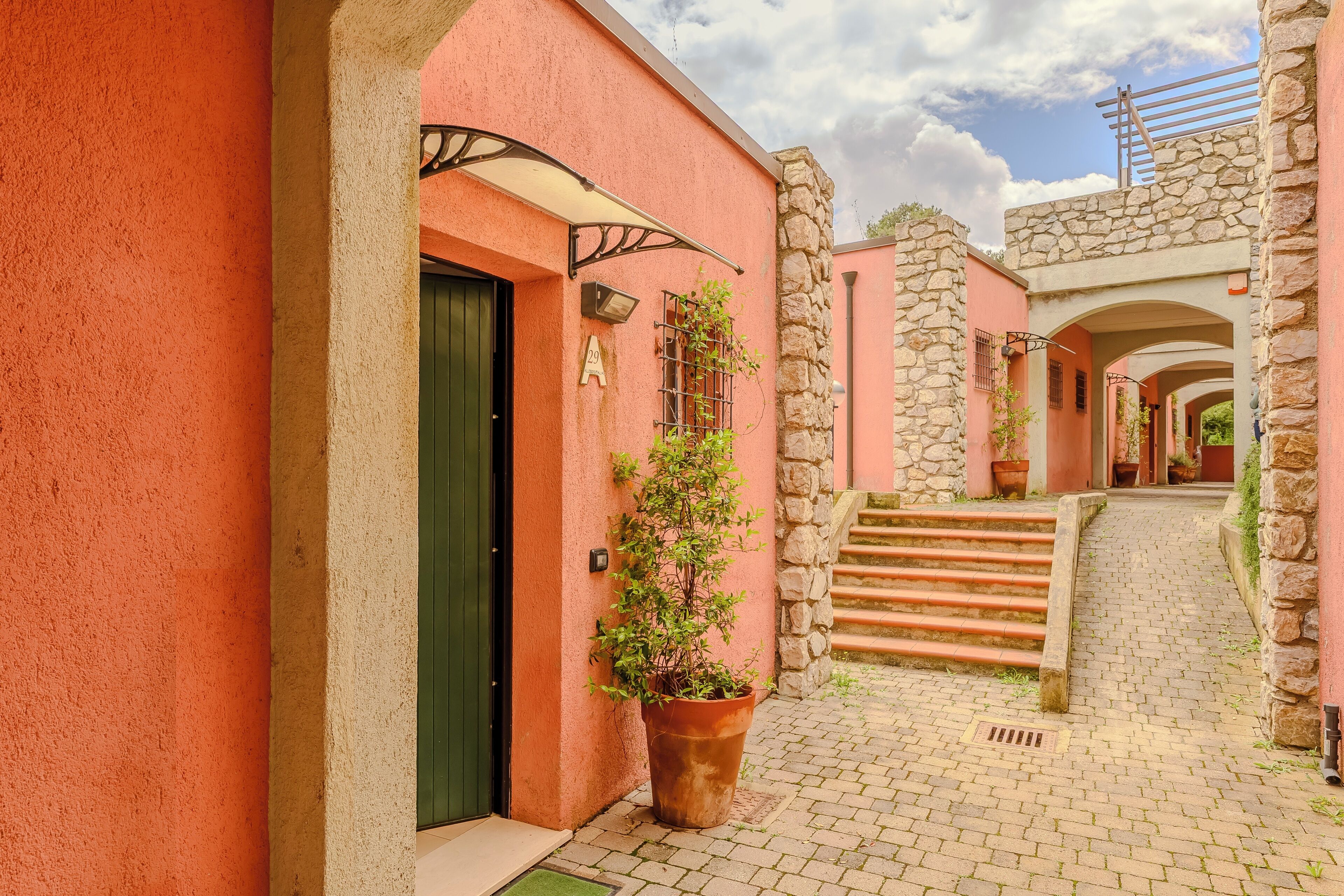 Um beco estreito com um edifício cor-de-rosa, paredes de pedra e um vaso de planta.