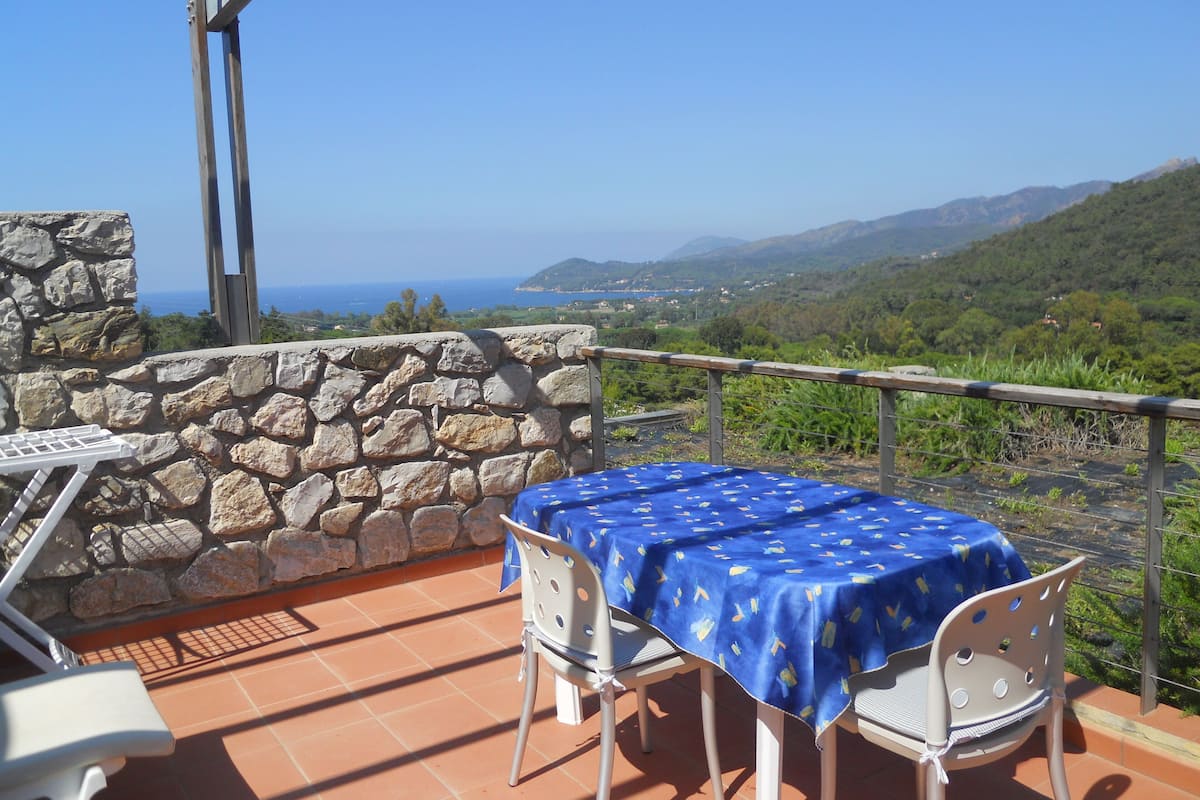 A terrace with a stone wall, a table with a blue tablecloth, and two chairs.