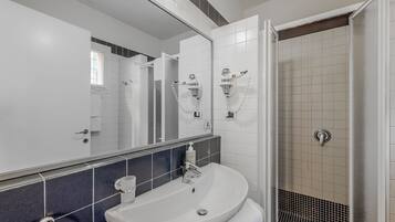 A modern bathroom with a white sink, a mirror, and a shower area.