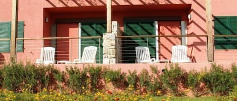 A building with a red facade, green shutters, and a covered outdoor seating area with white chairs.