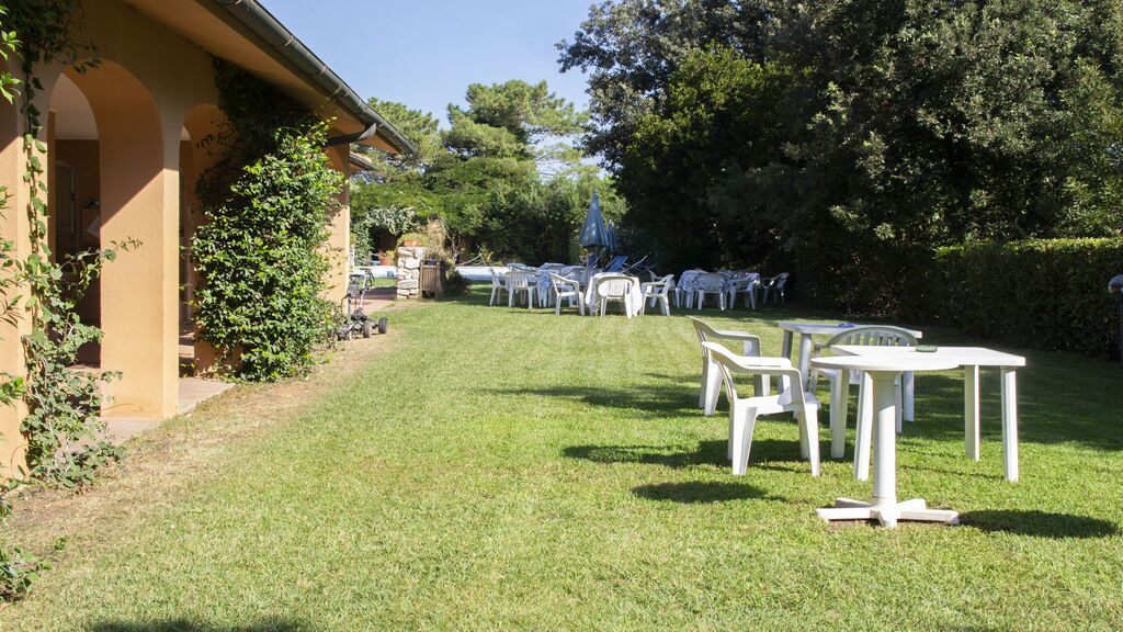 Un espace extérieur verdoyant, avec des tables et des chaises blanches disposées pour un événement.