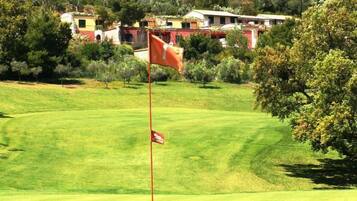 A golf course with a flagstick in the foreground, surrounded by well-maintained grass and trees.