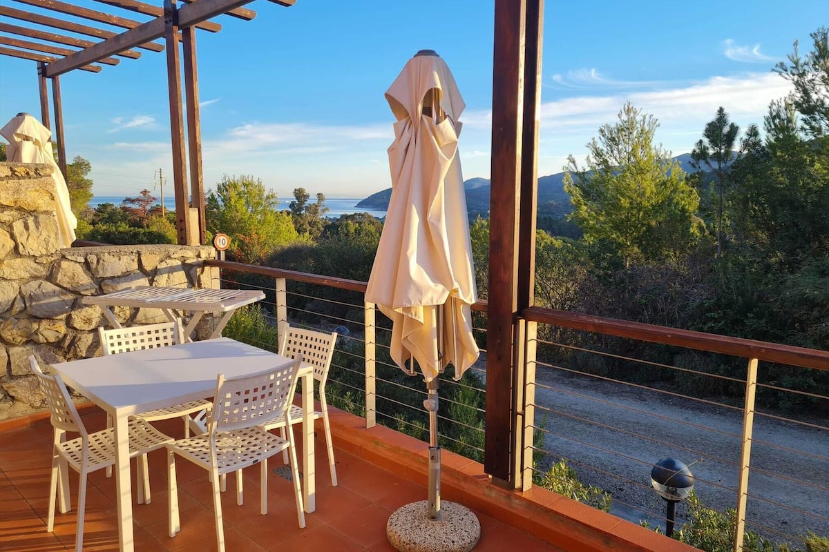 A balcony with a table and chairs, a covered umbrella, and a stone wall.