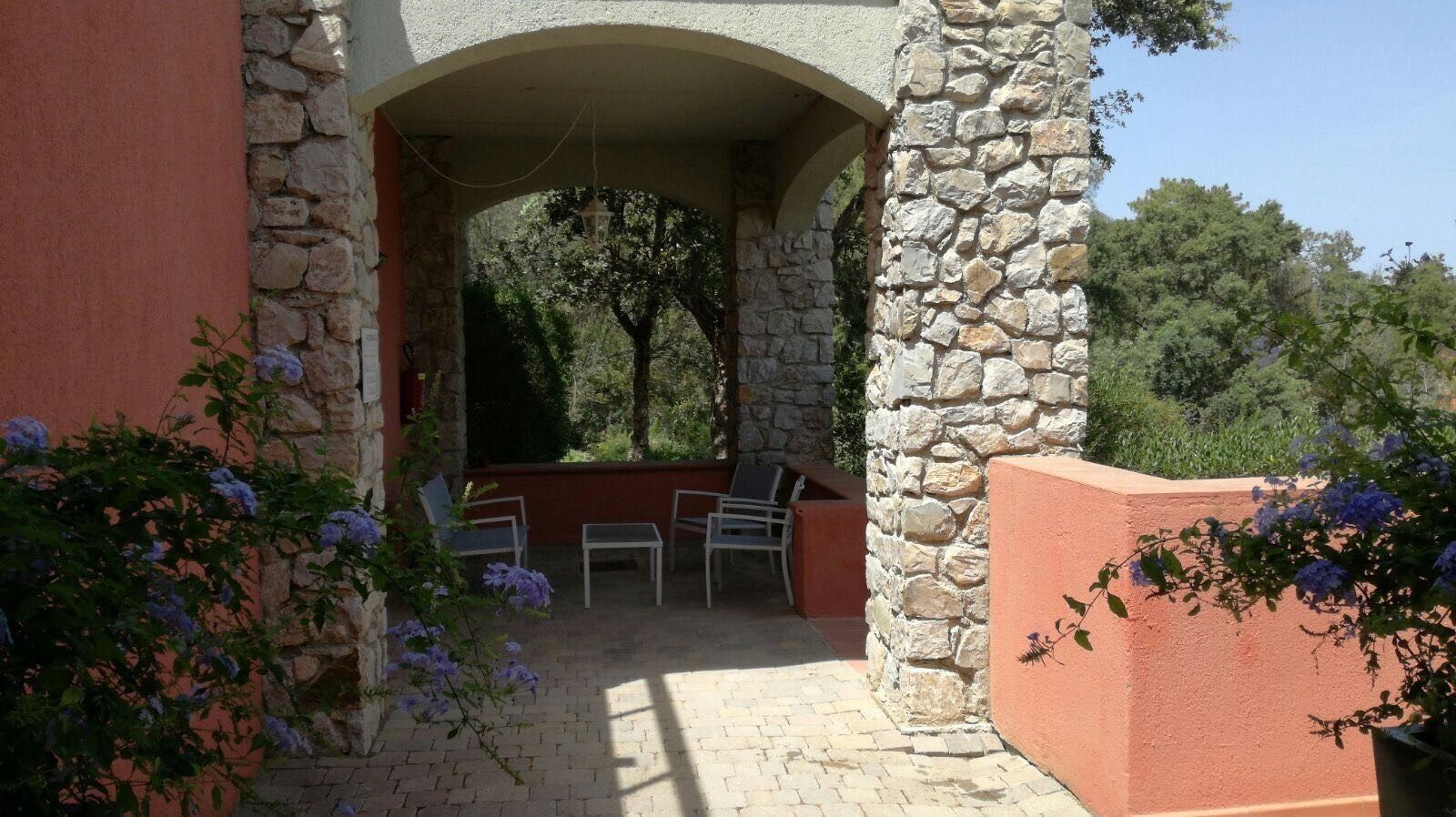 An outdoor patio with stone walls, a covered seating area, and a view of trees.