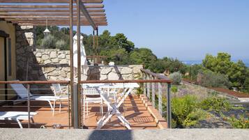 Une terrasse avec des chaises blanches et une table, d’où l’on peut admirer un paysage pittoresque, avec des arbres et une vue sur la mer.