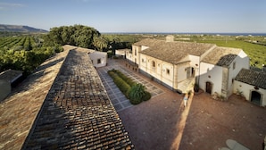 Une cour avec un toit en tuiles, un bâtiment blanc orné d’arches et une vue sur la campagne.