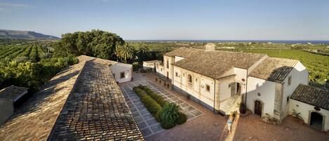 A courtyard with a tiled roof, a white building with arches, and a view of the countryside.