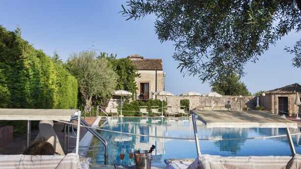 Un espace aménagé au bord de la piscine, avec des chaises longues, une petite table sur laquelle se trouvent un seau et des verres, et un bâtiment en arrière-plan.
