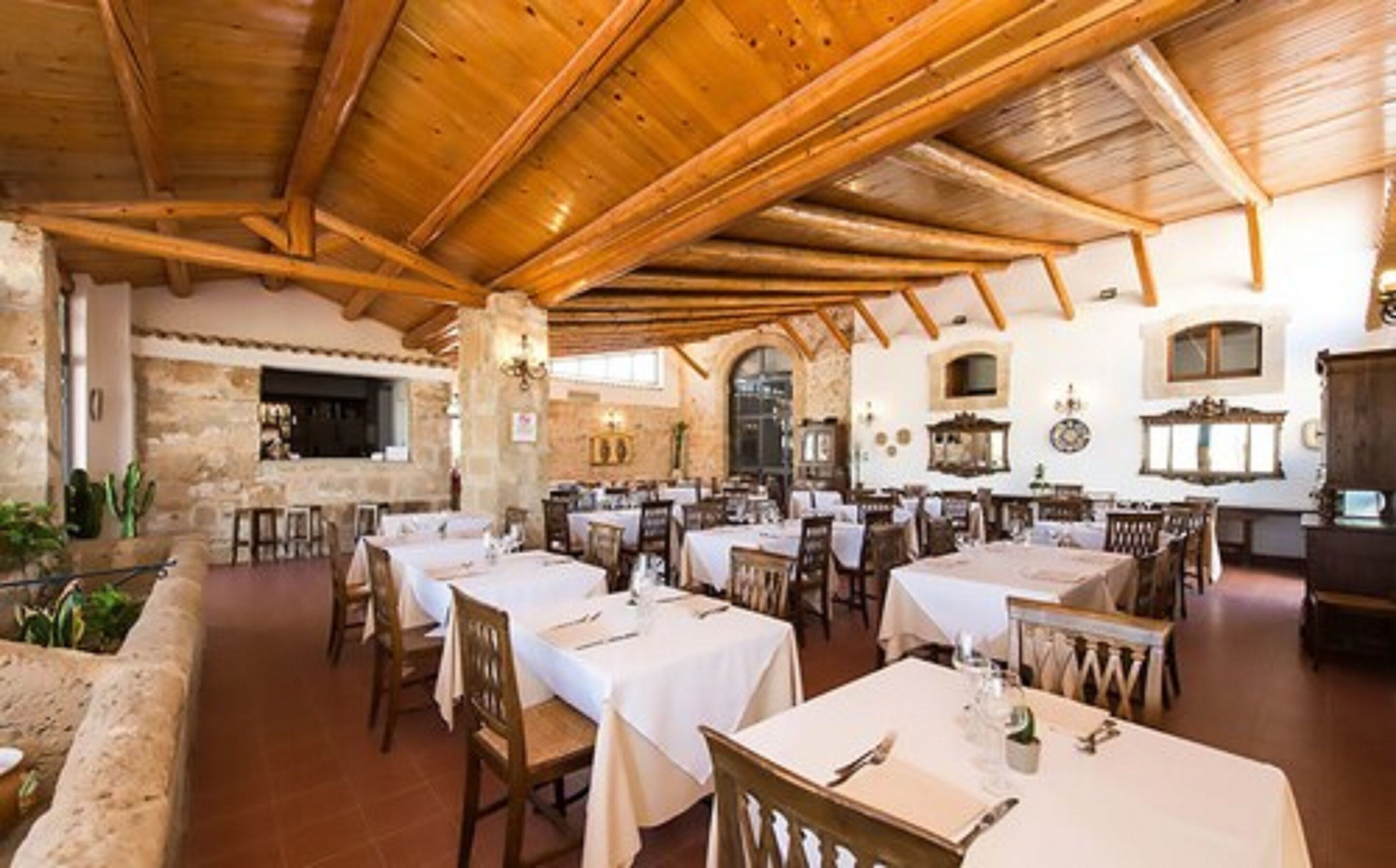Un comedor amplio con varias mesas y sillas, vigas de madera en el techo, paredes de piedra y un ambiente rústico.