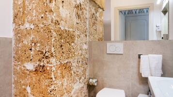 Une salle de bain avec un mur en pierre, des toilettes, un bidet et un lavabo avec un miroir.
