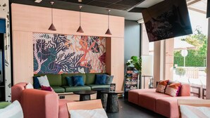 A modern lounge area with a green sofa, red armchairs, and a large abstract mural on the wall. - ibis Martigues (Martigues)