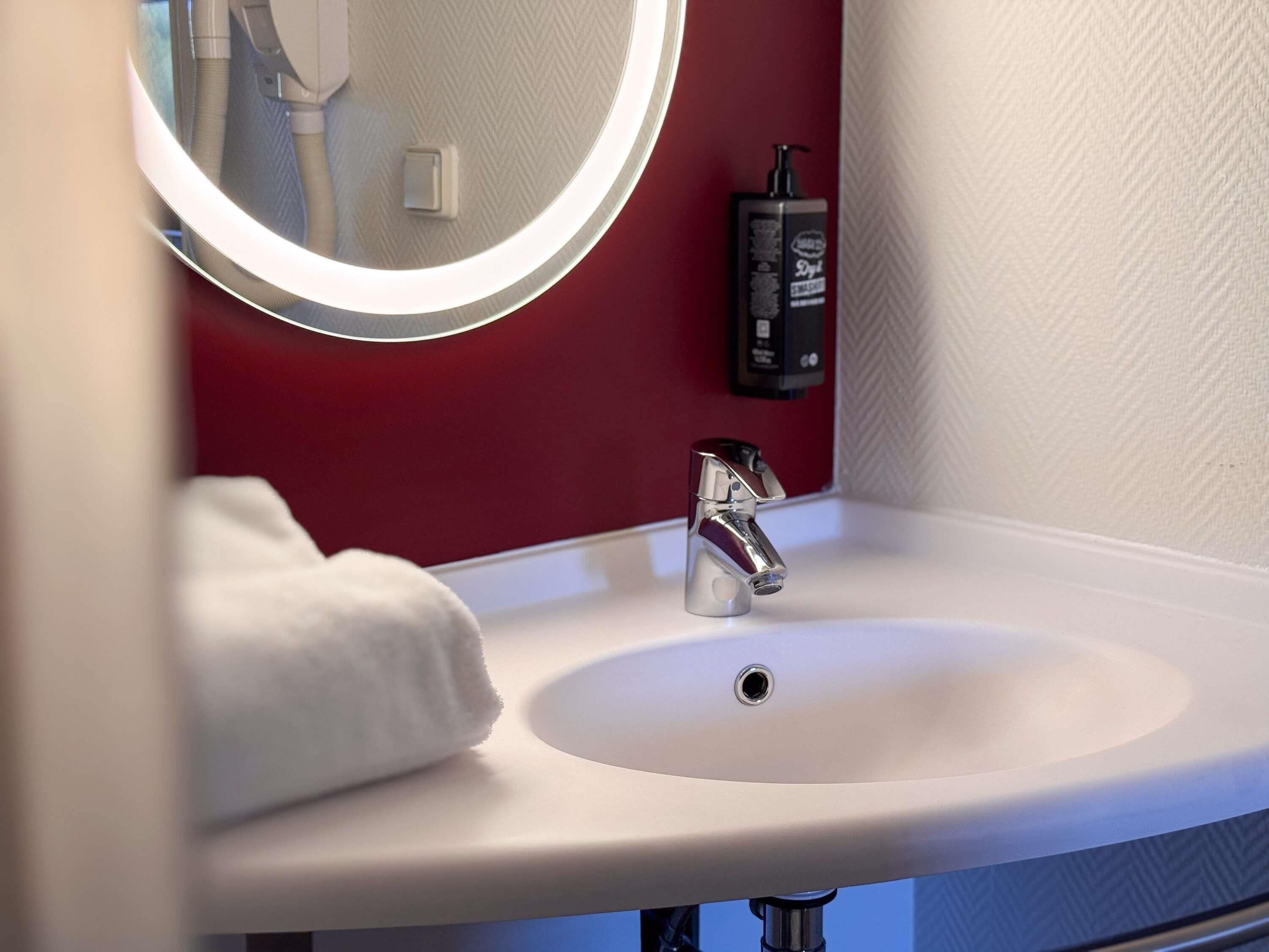 A bathroom sink with a mirror, a soap dispenser, and a towel.