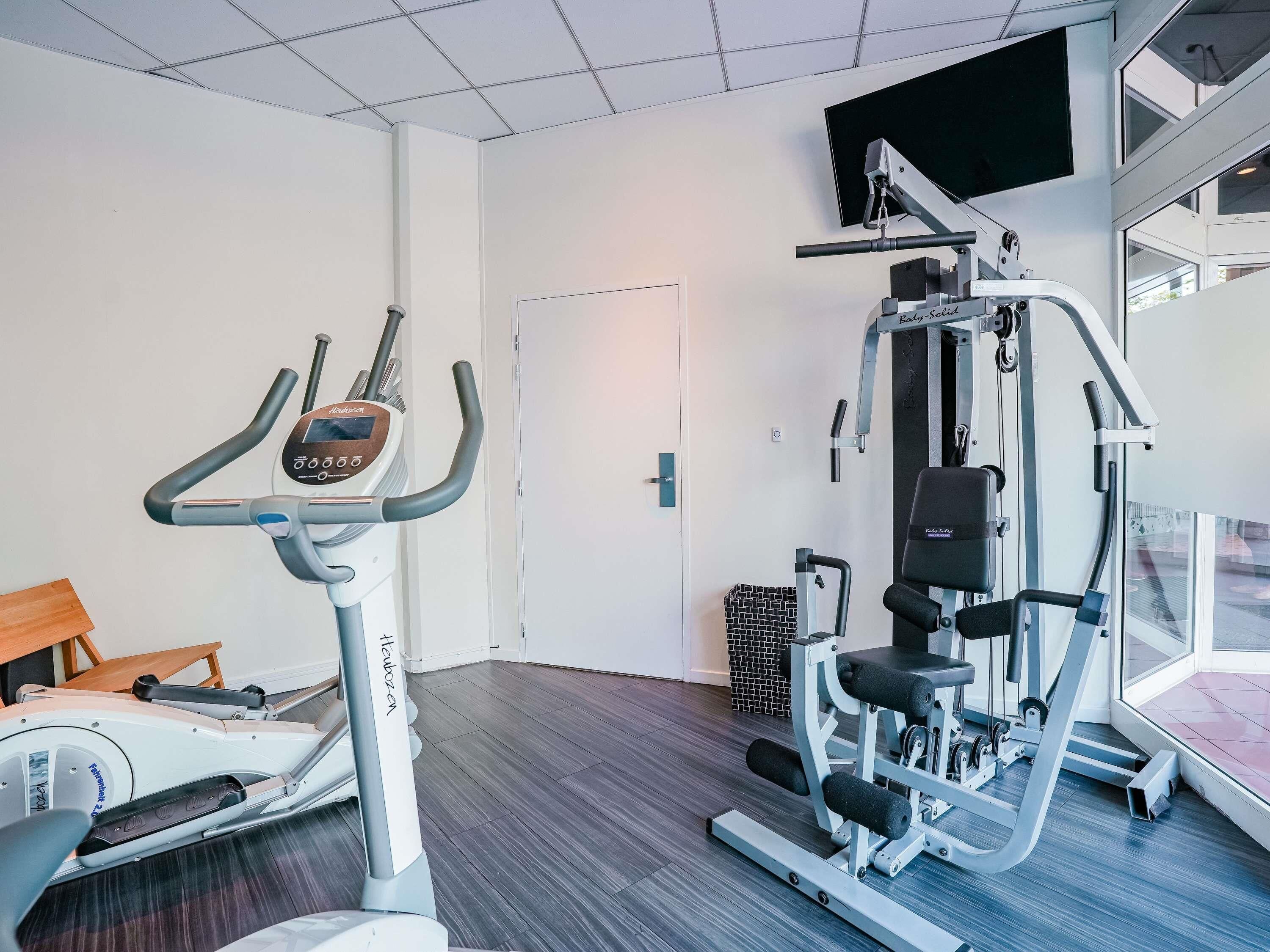 Un gimnasio con una máquina elíptica, una máquina de pesas y una banca.