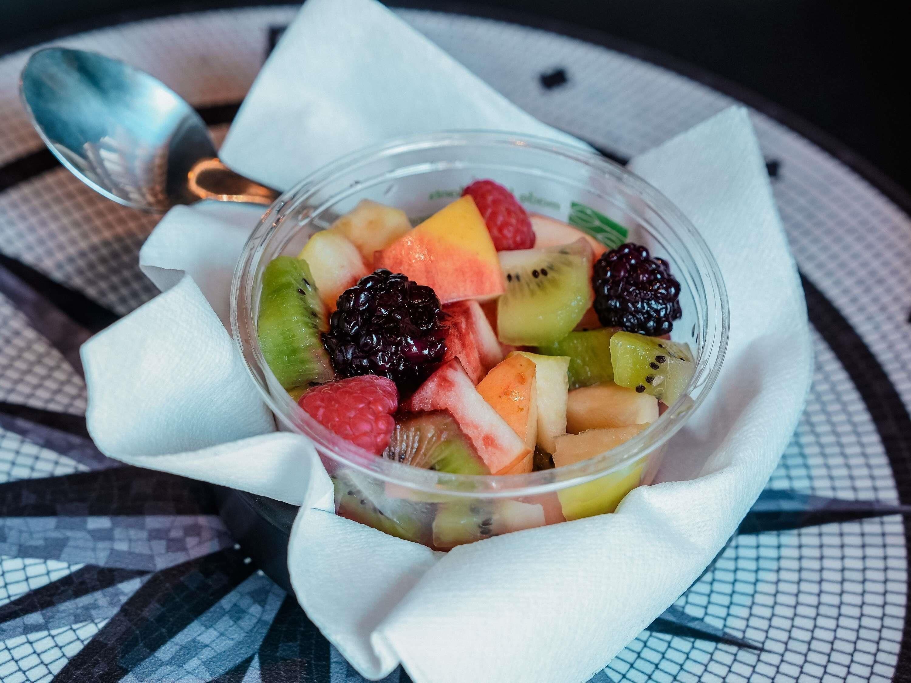 A clear glass bowl of assorted fruit salad on a patterned tablecloth.