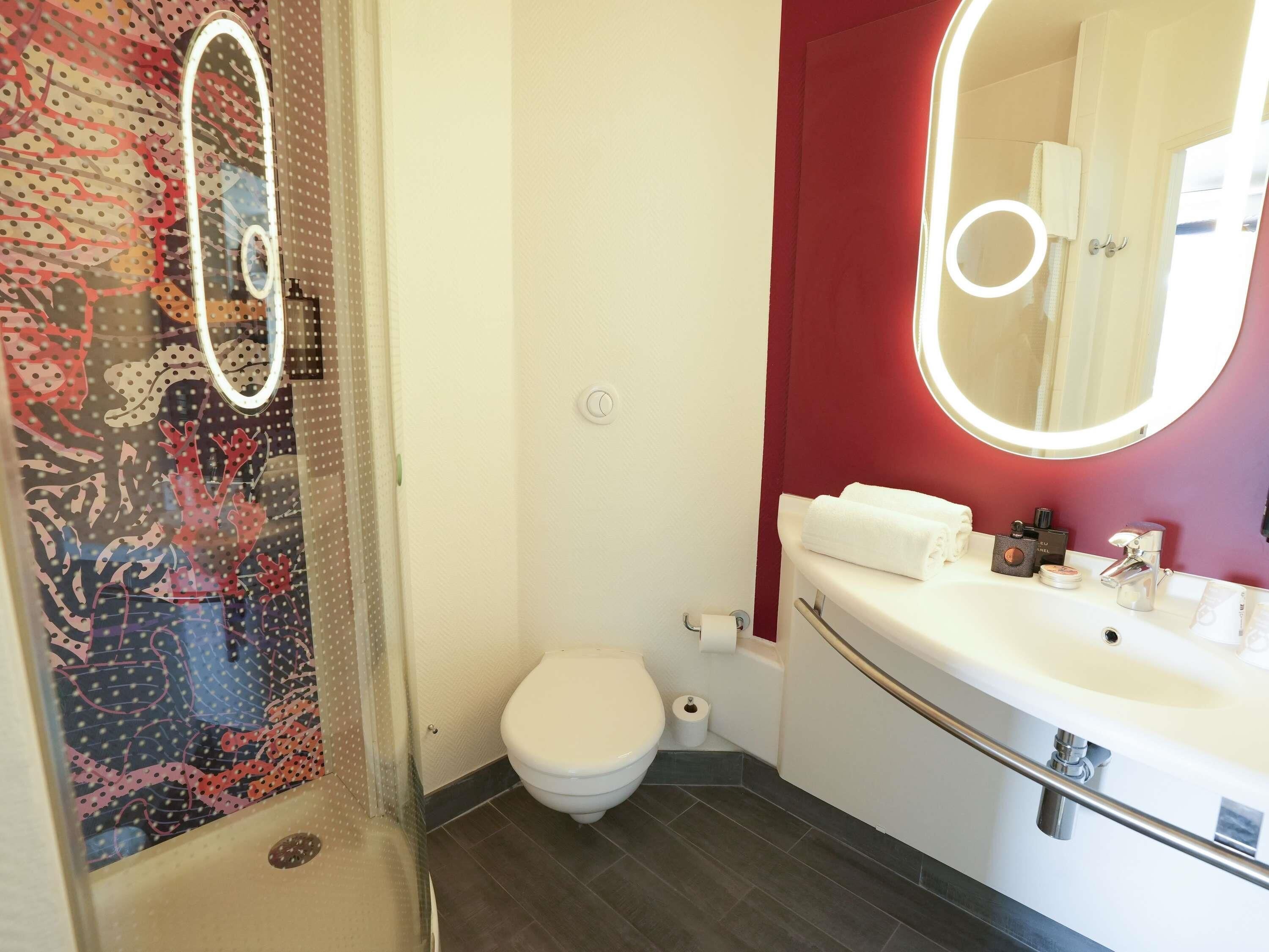 A bathroom with a toilet, a sink with a mirror, and a shower area.