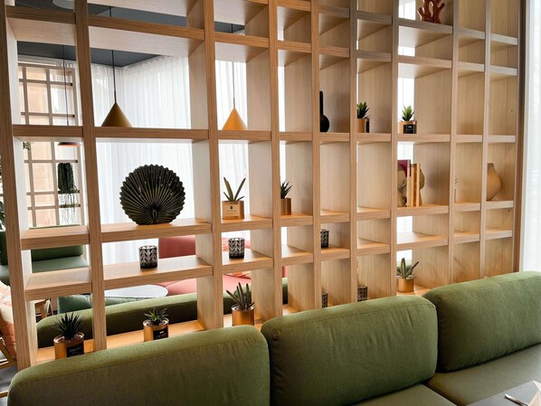 A room with a green sofa, wooden shelving with plants, and a window with white curtains. - ibis Martigues (Martigues)