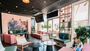 A modern interior with seating areas, a flat-screen TV, and large windows. - ibis Martigues (Martigues)
