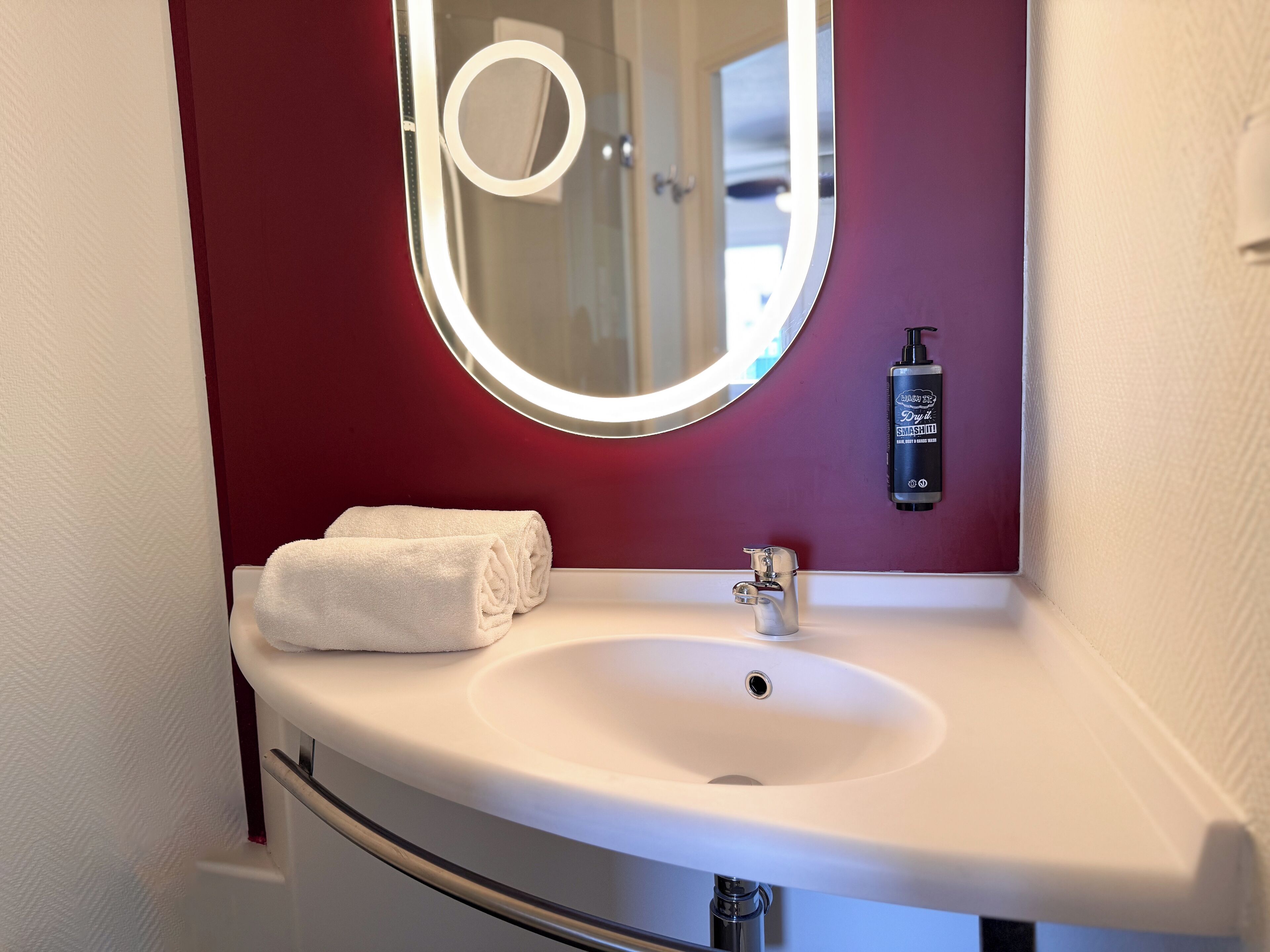 A bathroom with a white sink, a round mirror, and a red wall.
