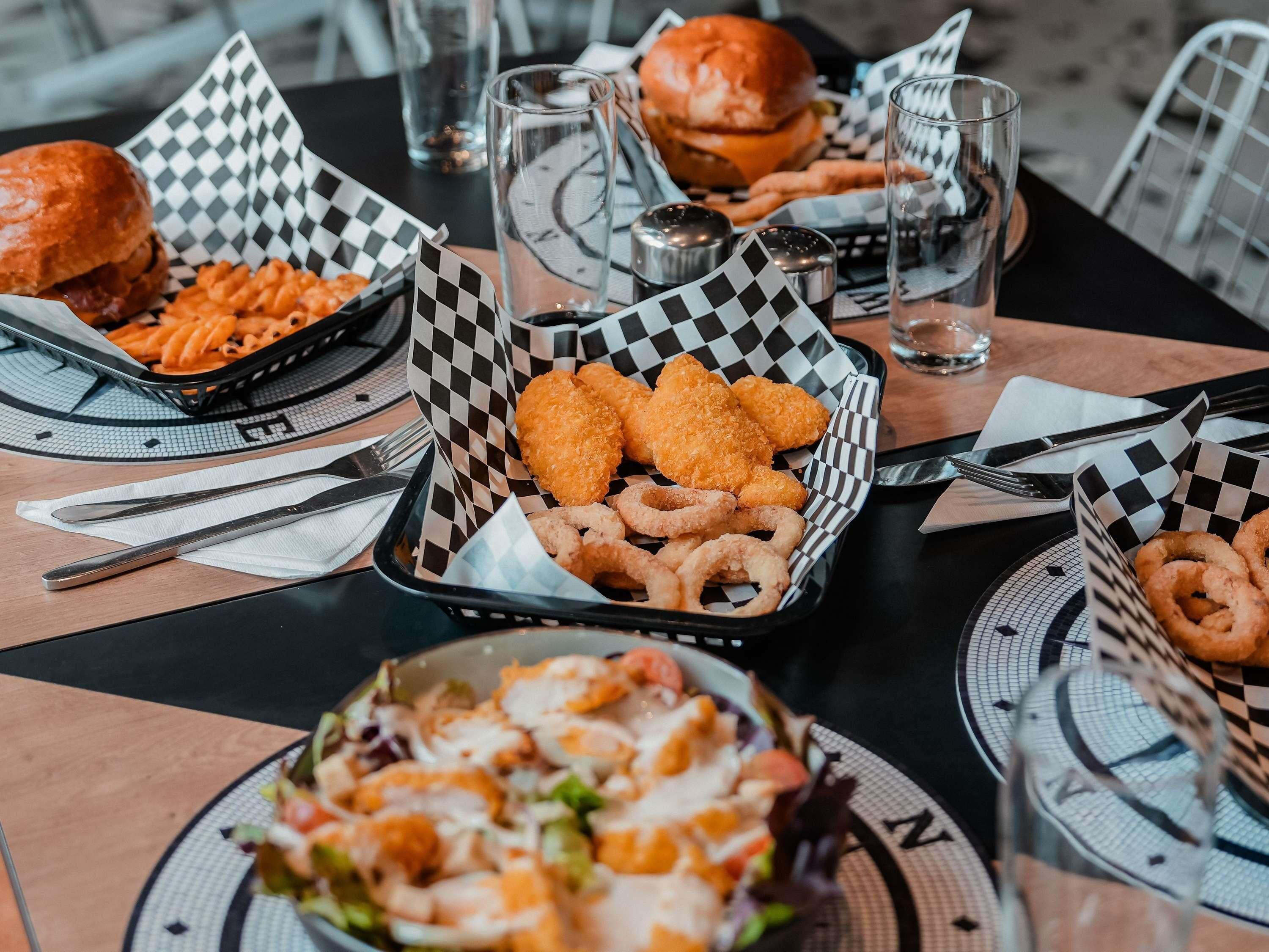 Une table dressée avec différents plats, notamment du poulet frit, des oignons frits et une salade.