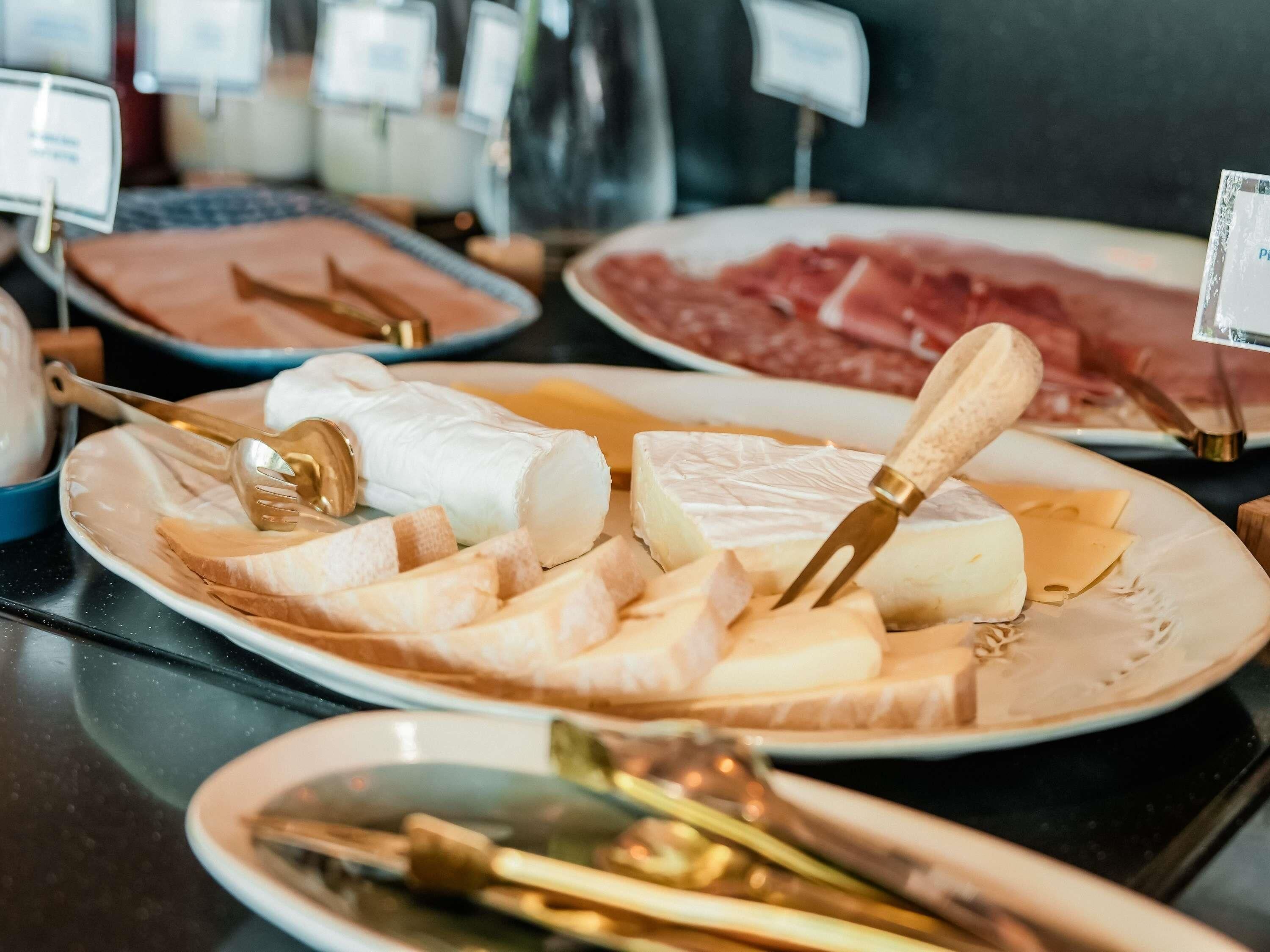 A buffet with various cheeses, meats, and utensils.