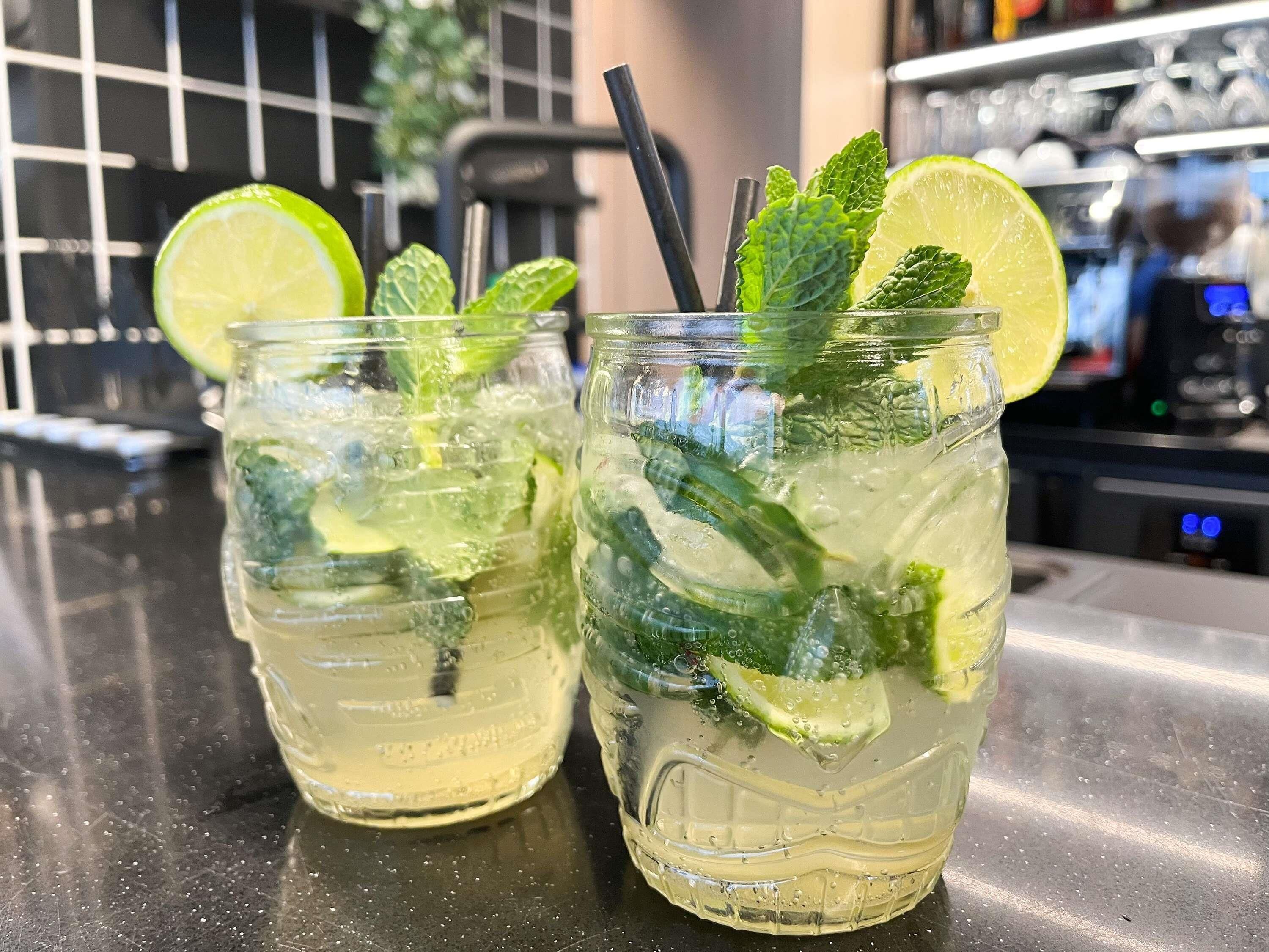 Two glasses of a beverage with lime and mint garnish, placed on a bar counter.